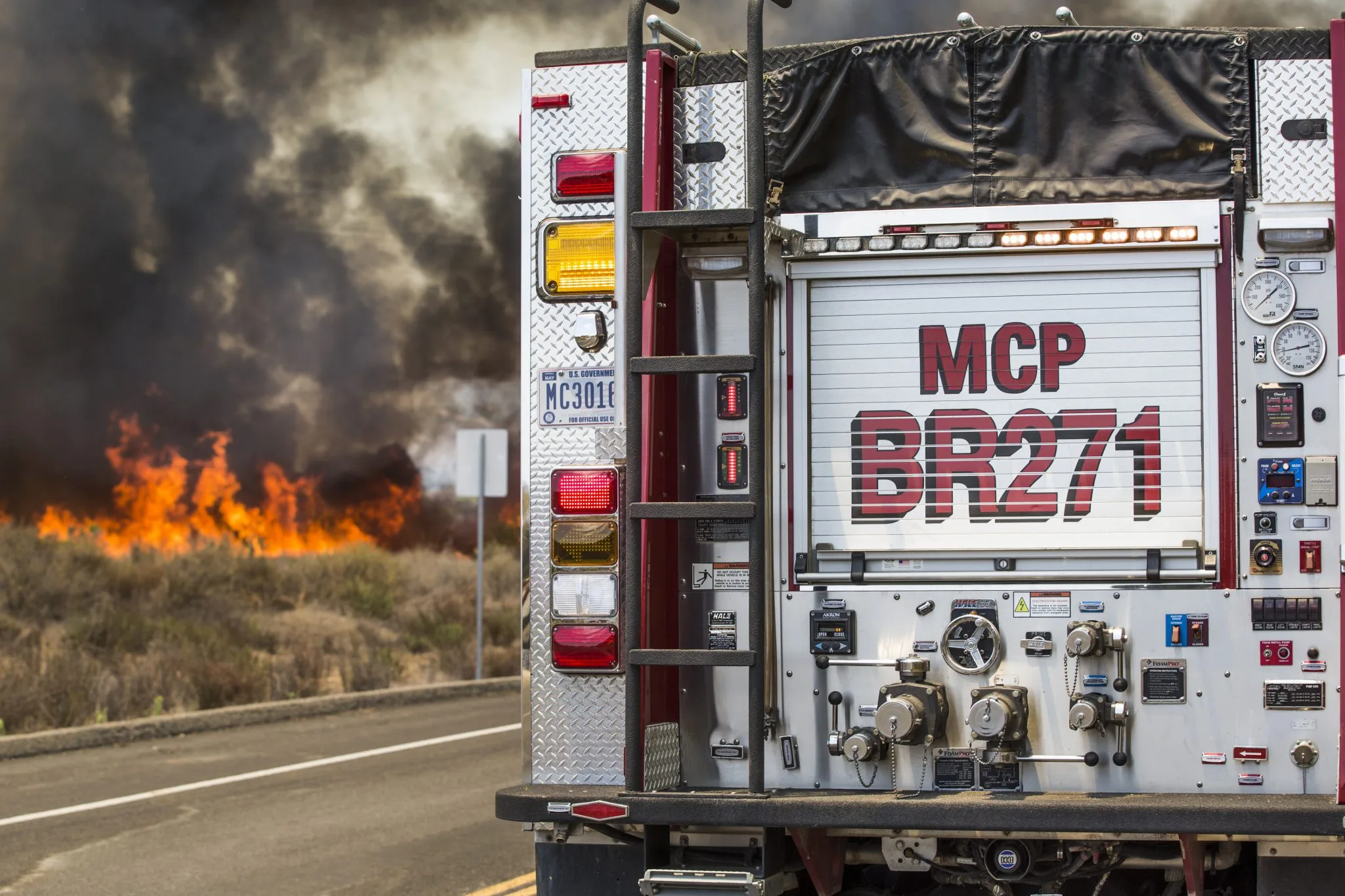 A fire engine is parked by the side of the road alongside a wildland fire. 